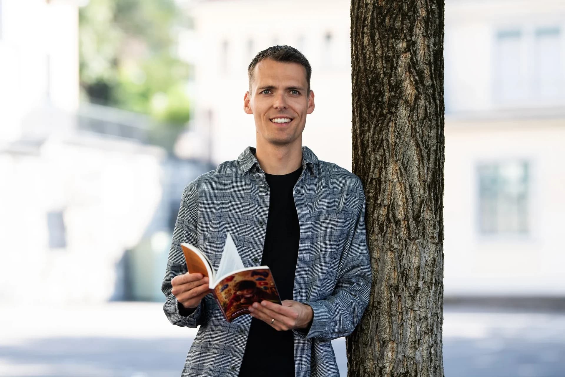 Lukas Jud steht mit einem geöffneten Buch neben einem Baum.